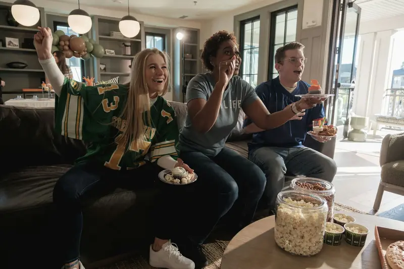 Des amis réunis au salon regardent un match de sport à la télévision.